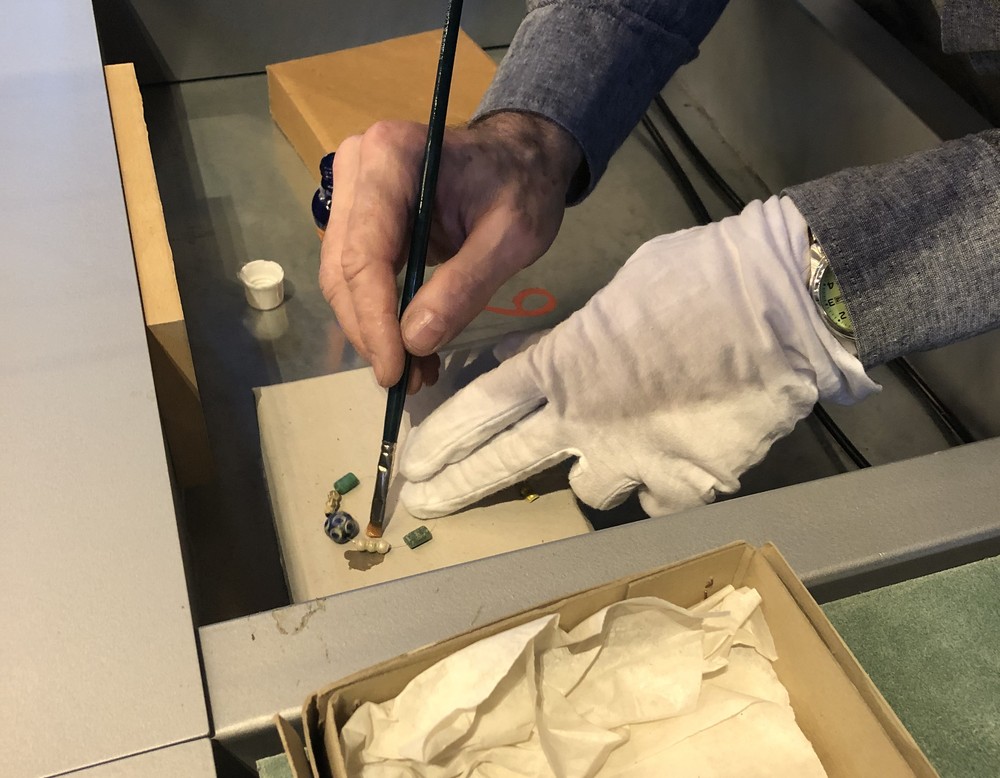 Mit einem Pinsel wird die Oberfläche der frühmittelalterlichen Glasperlen behandelt und vor weiterer Korrosion geschützt. (Foto: Streuber/ LWL)