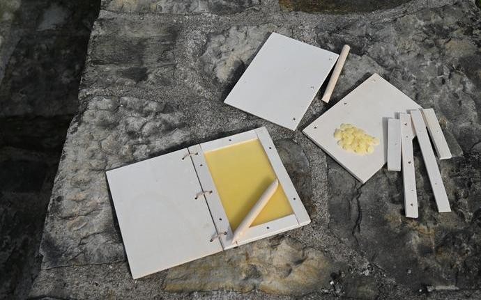 Eine fertig gebastelte Wachstafel und eine noch zu bastelnde Wachstafel auf einer Steinmauer.